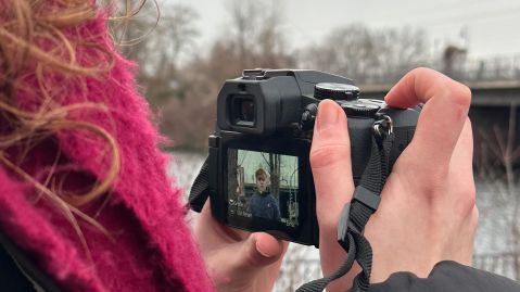 Eine Frauenhand hält eine Digitalkamera, auf deren Display eine Person zu sehen ist.
