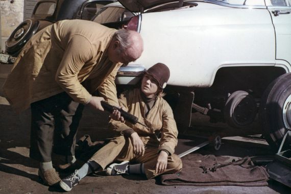 Ein Mann und eine Frau, die auf dem Boden sitzt, reparieren einen Autoreifen.