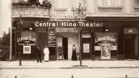 Three people and a dog in front of a cinema façade in Berlin, black and white photograph from 1910.
