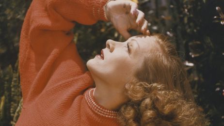 Marlene Dietrich in a red knitted sweater looks up at the sky.