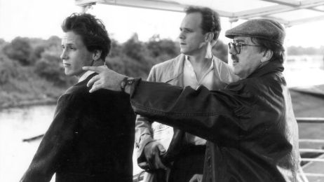 Black and white shot of director Heinrich Breloer during filming on a boat, pointing to the left while the two actors look in the same direction.