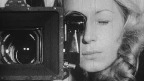 Black and white shot of a woman looking through the lens of a movie camera.