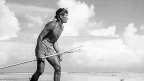 Black and white photograph of a man from the indigenous Polynesian population of Bora Bora on the beach, holding a spear.
